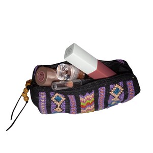 May include: A small, black zippered pouch with a colorful geometric pattern. The pouch is filled with various makeup items, including a lipstick, a lip gloss, and a small bottle of liquid.