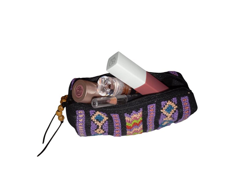 May include: A small, black zippered pouch with a colorful geometric pattern. The pouch is filled with various makeup items, including a lipstick, a lip gloss, and a small bottle of liquid.