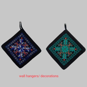 May include: Two black, square wall hangings with embroidered geometric designs. One features blue and red accents, the other teal and coral. Each has a loop for hanging. The text "wall hangers/ decorations" is at the bottom.