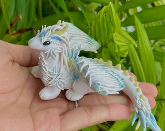 Op de afbeelding: Een wit en blauw keramiek drakenbeeldje met een gevederde textuur. De draak heeft een lange staart en vleugels, en zijn ogen zijn zwart.