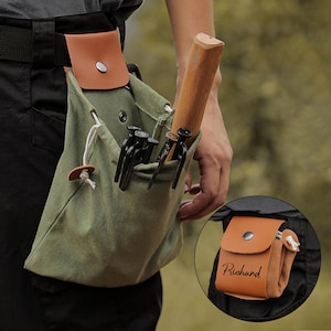 以下が含まれることがあります： オリーブグリーンのキャンバス製ツールバッグ。茶色の革製のフラップと巾着開閉式。バッグには、木製の柄のついたハンマーや黒い金属製の杭など、さまざまなツールが入っています。小さな茶色の革製のポーチも確認できます。