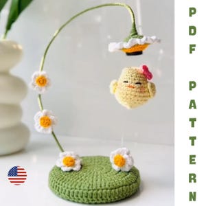 May include: A handmade crochet mobile featuring a yellow chick with a pink bow, suspended below a large flower. The mobile includes white daisies with yellow centers and a green base. The text "PDF PATTERN" is visible.