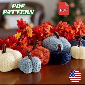 Peut inclure: Plusieurs citrouilles crochetées de couleurs crème, orange, bleu et marine, avec des tiges marron. Elles sont disposées avec des feuilles d'automne. Le texte "PDF PATTERN" et une icône "PDF" sont également présents.