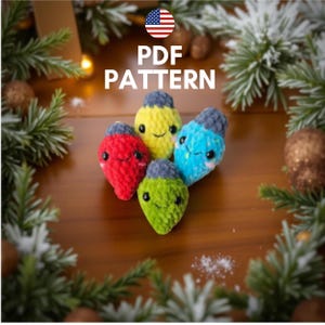May include: A collection of five colorful, crocheted Christmas light ornaments. The ornaments are red, yellow, blue, and green, each with a gray top and smiling face. The words "PDF PATTERN" are displayed above the ornaments, with an American flag icon.