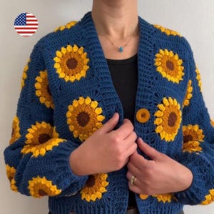 May include: A navy blue crochet cardigan with yellow and brown sunflower patterns. The cardigan has a button fastening and long sleeves. The floral design is repeated across the front and sleeves, creating a vibrant, handmade appearance.