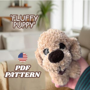 May include: A plush, tan-colored puppy with a dark brown nose and black eyes. The text "'FLUFFY PUPPY'" is above the puppy, and "PDF PATTERN" is below it, with an American flag graphic. The puppy is soft and fluffy.