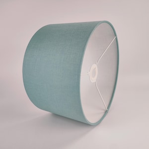 Puede incluir: Una pantalla de lámpara cilíndrica de color azul claro hecha de tela con un interior blanco.