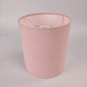 Peut inclure: Un abat-jour de lampe de couleur rose pâle en tissu. L'abat-jour est cylindrique et a un intérieur blanc.