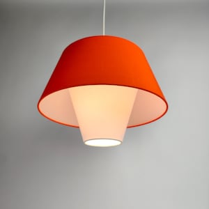 Op de afbeelding: Een moderne hanglamp met een feloranje buitenste kap en een witte binnenste kap. De lamp hangt aan een wit snoer.