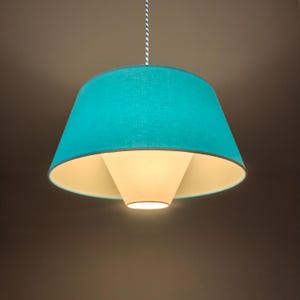 Op de afbeelding: Een turquoise hanglamp met een witte binnenkap. De lamp hangt aan een wit snoer.