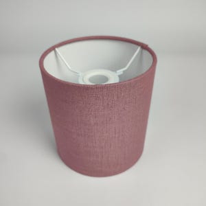 Peut inclure: Un abat-jour de lampe rose poussiéreux en tissu avec un intérieur blanc. L'abat-jour est cylindrique et a un design simple.