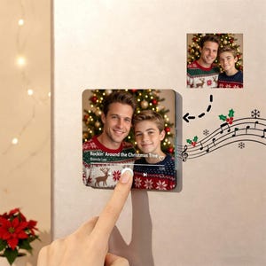 May include: A square acrylic plaque featuring a photo of two people wearing matching red and white patterned holiday sweaters in front of a Christmas tree. The plaque displays a music player interface with the text Rockin' Around the Christmas Tree.