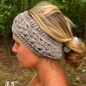 May include: A light brown crochet headband featuring a textured cable knit pattern. The headband has a width of 3.5 inches. The design includes a solid border at the top and bottom edges with a repeating braided stitch detail across the center.