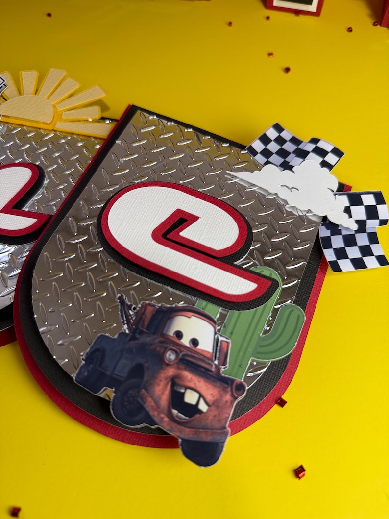 May include: A handmade banner with a race car theme. The banner features a silver diamond plate background, a large number "2" and "9" in red and white, and a cartoon image of a red tow truck. A checkered flag and a cactus are also included.
