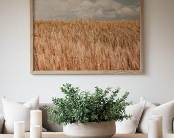 May include: A living room scene featuring a framed landscape print of a wheat field, a wooden coffee table, and a decorative arrangement. The table holds a large, round, light-colored planter with green foliage and white candles.