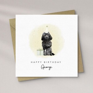 May include: A birthday card with a black dog wearing a party hat, beside a gift. The card reads "HAPPY BIRTHDAY George" in a handwritten font, set against a soft, yellow-green watercolour background. The card is in a brown envelope.