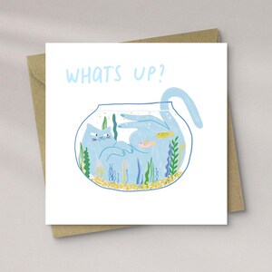 May include: A square greeting card with a blue cat inside a fishbowl, surrounded by aquatic plants and fish. The words "WHAT'S UP?" are written in light blue at the top. The card is on a brown envelope.