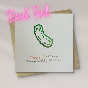 May include: A square white greeting card featuring a green glittery foil pickle illustration centred at the top. Below the pickle, the text reads "Happy Birthday to my little Pickle" in a dark, metallic-toned script font.
