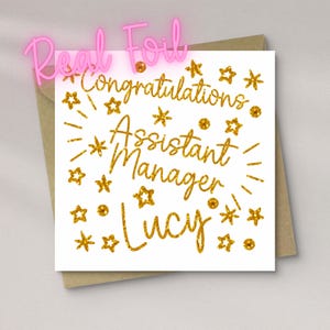 May include: A square white greeting card featuring gold foil text that reads Congratulations Assistant Manager Lucy. The design is decorated with various gold foil stars and circular dots scattered around the central text on the card front.