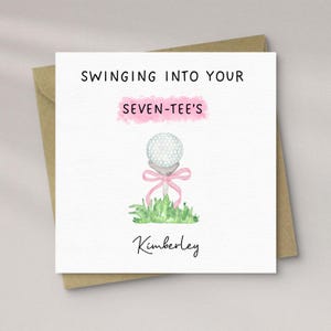 Könnte beinhalten: Quadratische Grußkarte mit Golf-Motiv. Sie zeigt eine Aquarell-Illustration eines Golfballs auf einem Tee mit rosa Schleife, in grünem Gras. Der Text enthält "SWINGING INTO YOUR SEVEN-TEE'S" und den Namen "Kimberley".