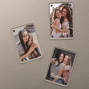 May include: Three rectangular clear acrylic magnets with photos of people. One magnet has the word "BFF", another has "MOH", and the third has "Bridesmaid" written on them. The magnets are on a gray surface.
