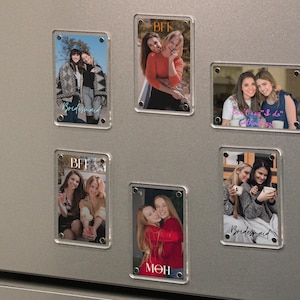 May include: Rectangular clear acrylic magnets with photos of people, attached to a silver refrigerator. Some magnets have the word "BFF" or "Bridesmaid" in script. The photos show groups of women in various settings, hugging and smiling.