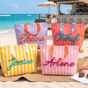 Peut inclure: Quatre sacs fourre-tout rectangulaires à rayures verticales bleu et rose, orange et rose, jaune et blanc, et rose clair et blanc. Chaque sac porte un prénom en lettres cursives en relief : Edwina, Cheryl, Jessica et Arlene.