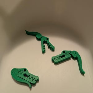 Puede incluir: Tres clips de plástico verde en forma de cocodrilo. Los clips son articulados y tienen una superficie texturizada.