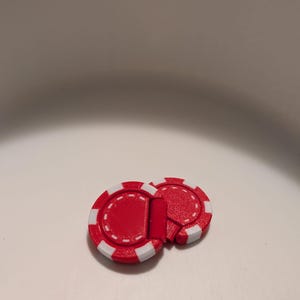 May include: Two red and white poker chip-shaped objects. The chips have a red centre with a white border and a dotted pattern. These are likely game accessories, possibly for poker or other casino-style games.