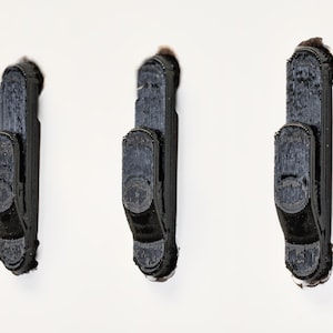 May include: Three black plastic hooks mounted on a white wall.
