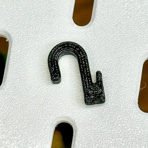 May include: A black plastic hook with a rounded top and a pointed end. The hook is designed for hanging items.