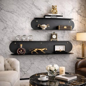 Może przedstawiać: Trzypoziomowe czarne półki ścienne z elementami dekoracyjnymi. Górna półka zawiera złotą figurkę misia i książki. Środkowa półka ma dekoracyjny wazon i małe pudełko. Dolna półka prezentuje butelkę, złotą statuetkę pantery i pudełko na biżuterię.