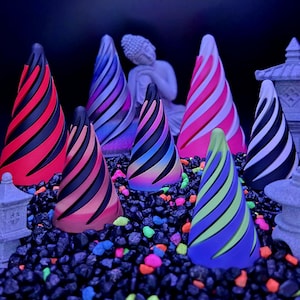 May include: A collection of colorful, cone-shaped decorative objects with spiral designs. The cones feature a variety of colors, including red, pink, blue, and green, and are set against a dark background with a Buddha statue and small decorative structures.