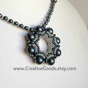 以下が含まれることがあります： 濃い青と銀色のビーズネックレスで、円形のペンダントが付いています。ペンダントはより小さなビーズで作られており、中央に穴が開いています。