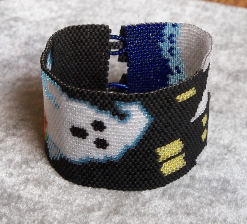 May include: A black beaded bracelet with a white and blue design. The bracelet features a pattern of ghosts with black eyes and a yellow stripe.