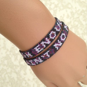 May include: Two beaded bracelets with a geometric pattern in black, white, and pink. The bracelets are worn on a person's wrist.