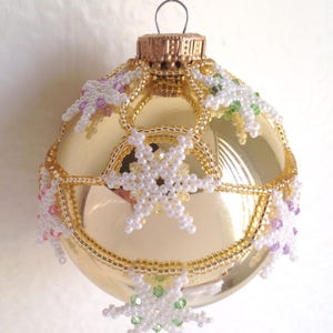 May include: A gold glass Christmas bauble decorated with white, pink, green and purple beaded snowflakes.