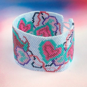 Puede incluir: Un brazalete de cuentas azul claro con un patrón floral en rosa, turquesa y morado.