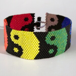 Pode incluir: Um bracelete de contas coloridas com um design yin yang. O bracelete é feito de contas pretas, vermelhas, amarelas, verdes, azuis e roxas.