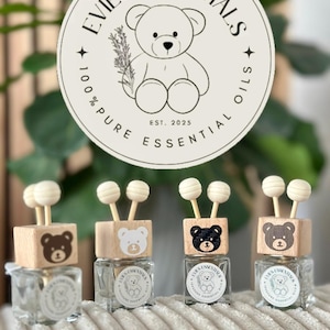 May include: Four glass essential oil diffusers with wooden tops featuring bear designs. Each diffuser has a wooden stick with a white ball on top. The logo reads "Evie's Essentials 100% Pure Essential Oils Est. 2025".