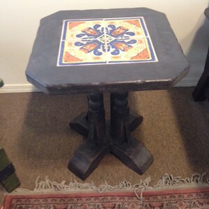 May include: A dark brown wooden end table with a square top featuring a colorful tile design. The table has a four-legged base with a unique, decorative design.