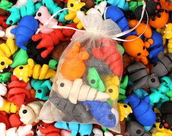May include: A collection of colorful, small animal-shaped erasers in various colors, including red, blue, yellow, and green. A sheer bag contains a selection of the erasers. The erasers are scattered, creating a playful and vibrant scene.