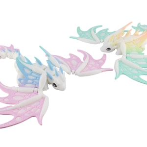 May include: Two articulated dragon toys in pastel colors. One dragon features pink and blue wings, while the other has mint green and yellow wings. The dragons have white bodies and small black eyes, with a fantasy theme.