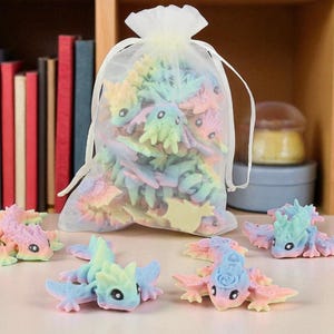 May include: A selection of pastel-coloured dragon figurines, some scattered on a surface and others inside a sheer drawstring bag. The dragons are in shades of pink, blue, yellow, and green. A bookshelf with colourful books is in the background.