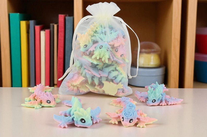 May include: A selection of pastel-coloured dragon figurines, some scattered on a surface and others inside a sheer drawstring bag. The dragons are in shades of pink, blue, yellow, and green. A bookshelf with colourful books is in the background.