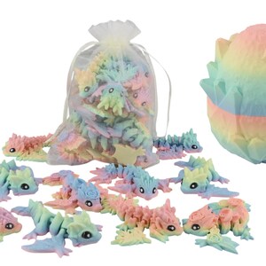 May include: A selection of pastel-coloured dragon figurines and a large, matching egg-shaped sculpture. The dragons are in various poses, some inside a sheer bag. The egg is multi-layered with a textured surface, showcasing a rainbow of colours.