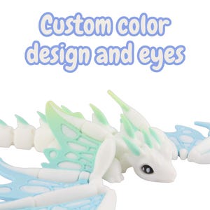 May include: A white articulated dragon toy with light blue and green accents. The text "Custom color design and eyes" is displayed above the dragon. The dragon has a detailed design with wings and a long tail.