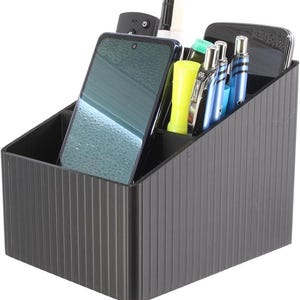 May include: A black desk organizer with vertical ribbed detailing. The organizer holds a smartphone, pens, a remote control, and other office supplies. The organizer is designed to keep items organized and accessible.