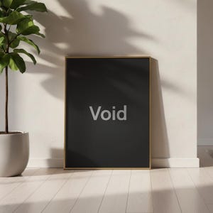 May include: A framed black art print with the word "Void" in a light gray font. The frame is gold-colored. The print is leaning against a white wall, with a potted plant and wooden floor in the background.