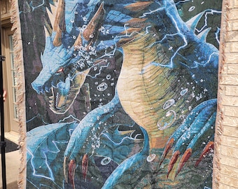 May include: A woven tapestry blanket featuring a detailed illustration of a blue dragon with lightning effects. The dragon has sharp claws and teeth, with a green and blue background. The blanket has a fringed edge.